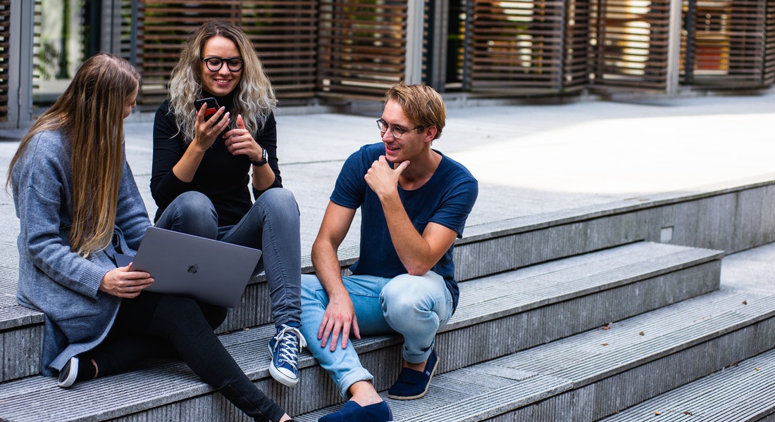 Female and male students sitting outside the university chatting and enjoying student life at UCPH